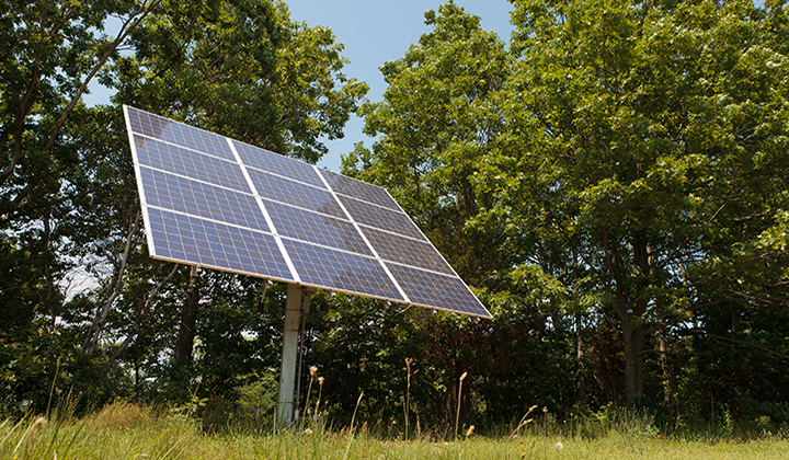 Rotating solar panel in a field set against a wooded area.