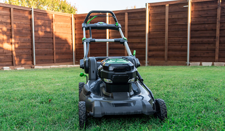 Front view of electric mower in fenced in backyard with green grass.