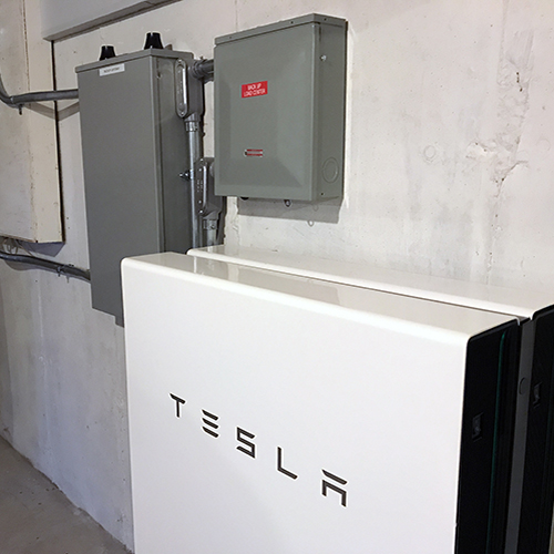 Side angle of Tesla powerwall and electrical connections in basement.