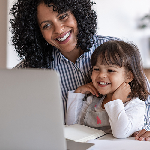 Busy mother smiling while working on a laptop with her cute little girl sitting on her lap