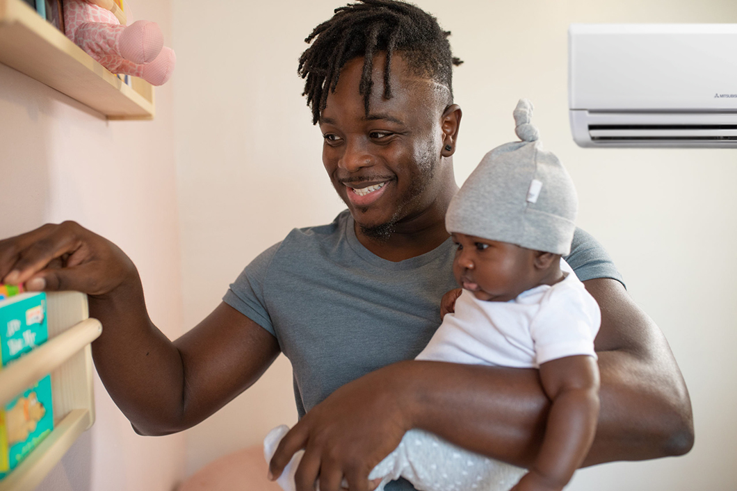 Dad with baby in his arms at home, heat pump on the wall and comfortable in his home.