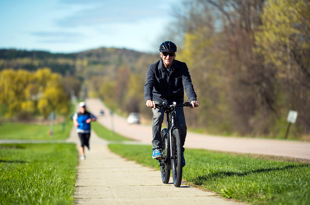 Man riding electric bike on Vermont road with runner in the background.