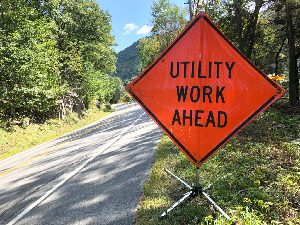 Orange diamond sign that reads 'Utility Work Ahead' on the side of a road