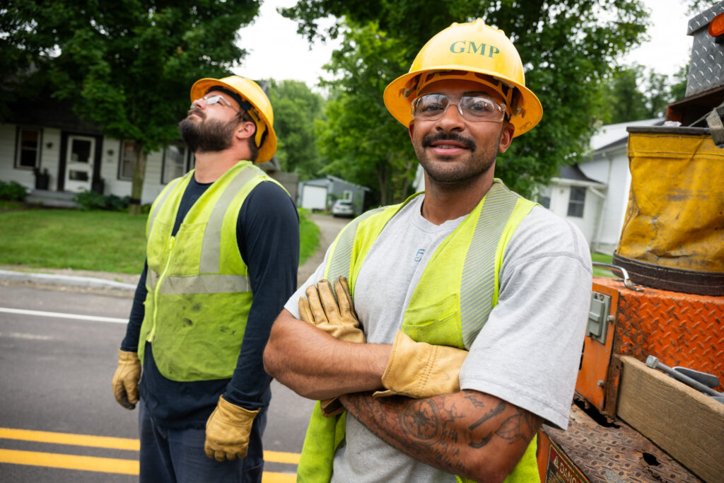 Two lineworkers with yellow GMP hardhats, yellow vests and gloves